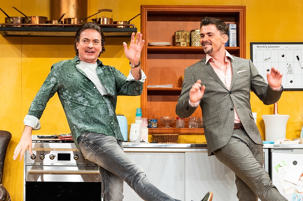 Zwei Männer tanzen vor einer Küche als Theaterkulisse