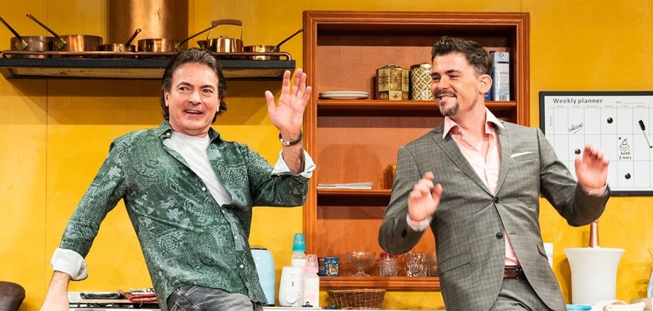 Zwei Männer tanzen vor einer Küche als Theaterkulisse