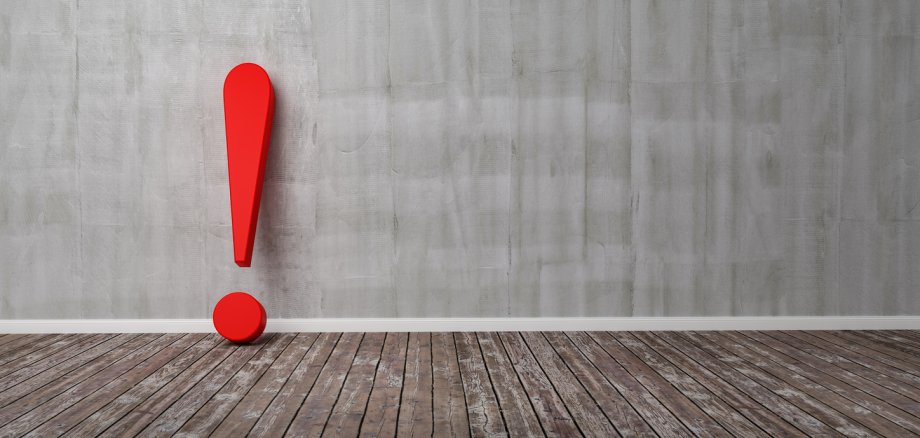 Rotes Ausrufezeichen Plastisches rotes Ausrufezeichen an einer hellbraunen Wand lehnend