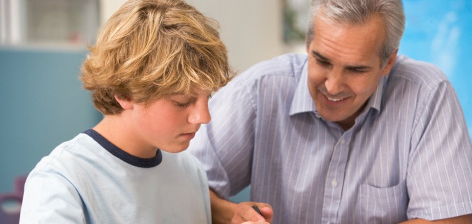 Lehrer und Schüler beugen sich über Schulheft
